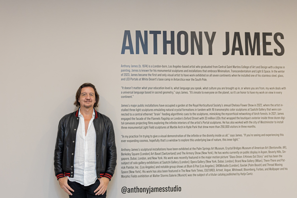 Anthony James de pie junto a un mural en donde es posible leer su biografía (en inglés)