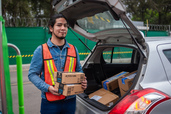 Repartidos de Amazon Flex con la cajuela del auto abierta y sosteniendo un paquete de la marca