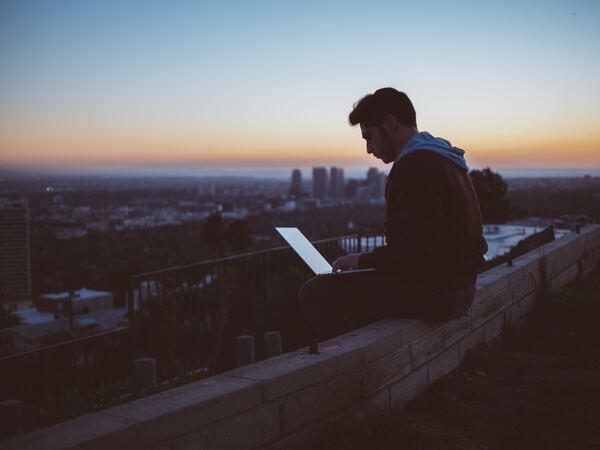 Joven trabajando en el atardecer, en la azotea, con su laptop