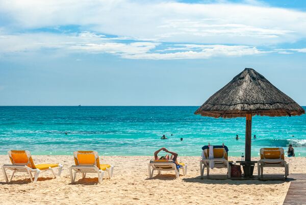 La playa de Cancún con unos camastros y una palmera en primer plano