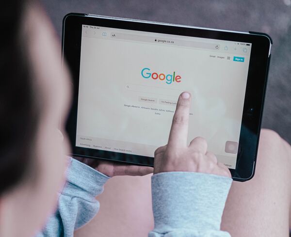 Hombre con una tablet en el regazo, en la pantalla de la table se ve el buscador de google