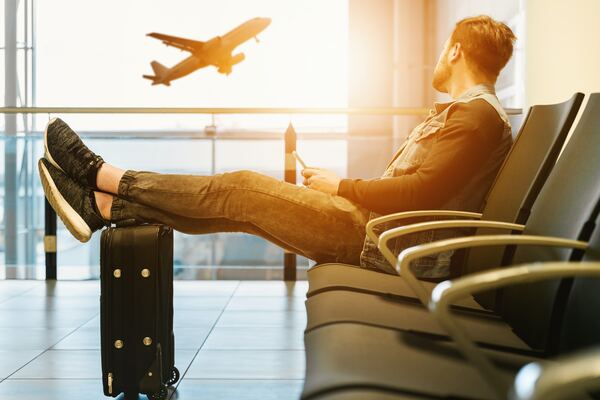 Hombre joven mira los ventanales de un aeropuerto mientras un avión sobrevuela la zona