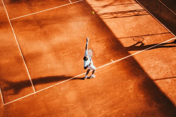 Hombre jugando tenis en una cancha de color rojo