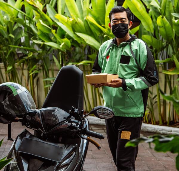 Repartidor con traje verde junto a su motocicleta de color negro