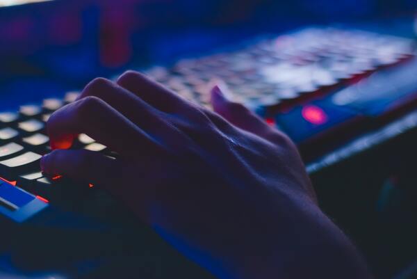 Un par de manos escribiendo en un teclado iluminado por luces led