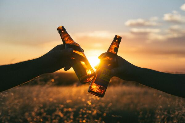 Dos personas diciendo "salud" al estrechar los envases de sus cervezas